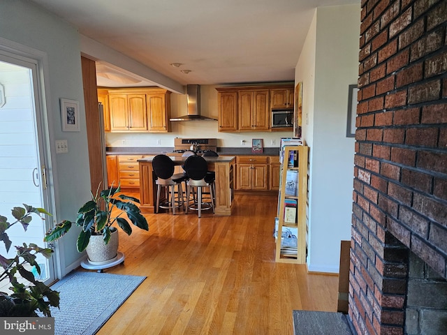 kitchen featuring stainless steel appliances, a kitchen bar, light hardwood / wood-style flooring, and wall chimney range hood