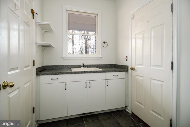 kitchen with dark tile patterned floors, white cabinetry, and sink