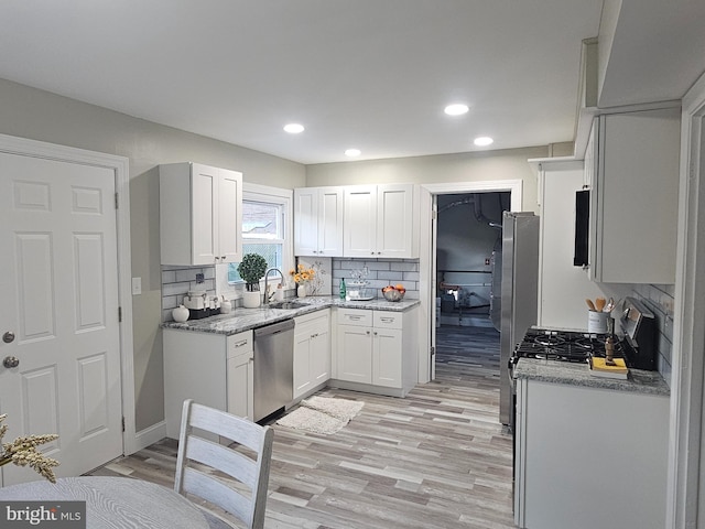 kitchen with white cabinetry, sink, light stone counters, decorative backsplash, and appliances with stainless steel finishes