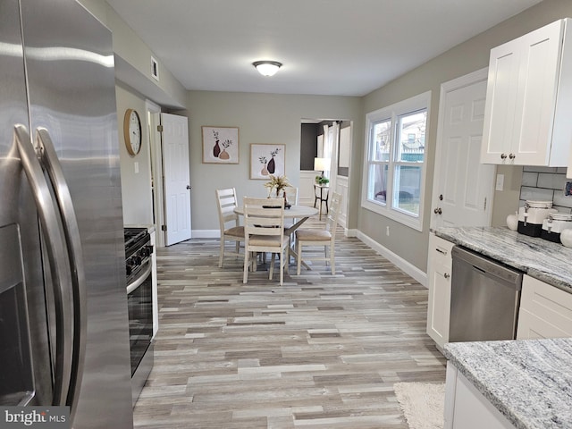 kitchen featuring light hardwood / wood-style flooring, decorative backsplash, light stone countertops, white cabinetry, and stainless steel appliances