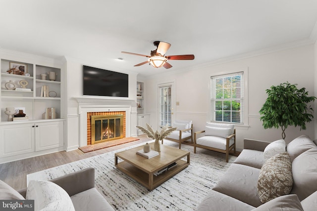 living room featuring a fireplace, light hardwood / wood-style flooring, crown molding, built in shelves, and ceiling fan