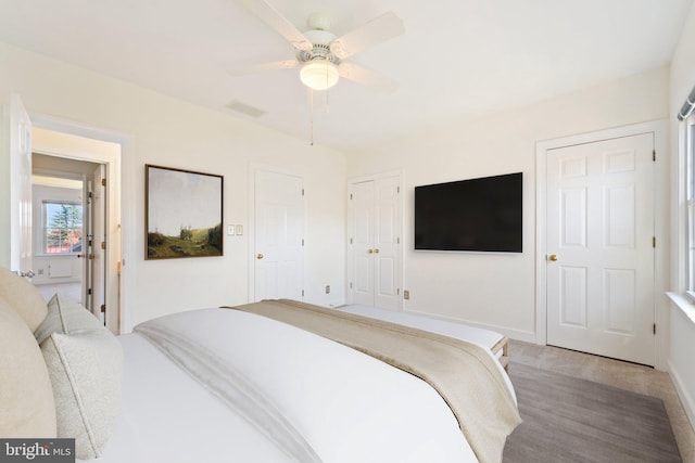 bedroom with light hardwood / wood-style flooring, two closets, and ceiling fan