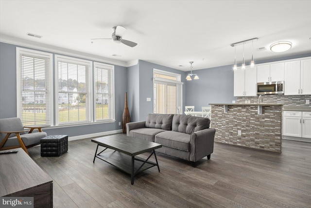 living room featuring ornamental molding, dark wood-type flooring, and ceiling fan with notable chandelier