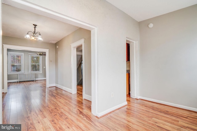 empty room featuring a notable chandelier, radiator heating unit, and light wood-type flooring