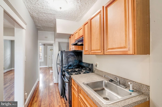 kitchen featuring sink, stainless steel range with gas cooktop, a textured ceiling, and light wood-type flooring