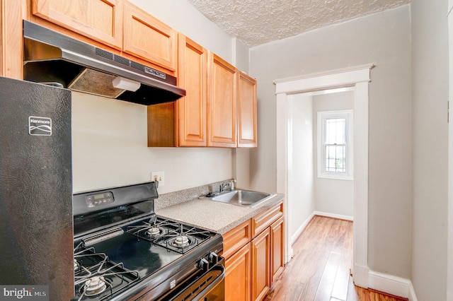 kitchen with sink, light wood-type flooring, a textured ceiling, black gas range oven, and light brown cabinets