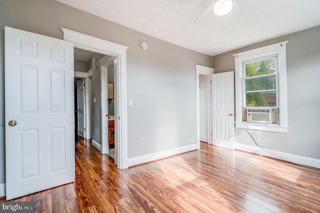 unfurnished bedroom featuring ceiling fan, a textured ceiling, cooling unit, and dark hardwood / wood-style floors