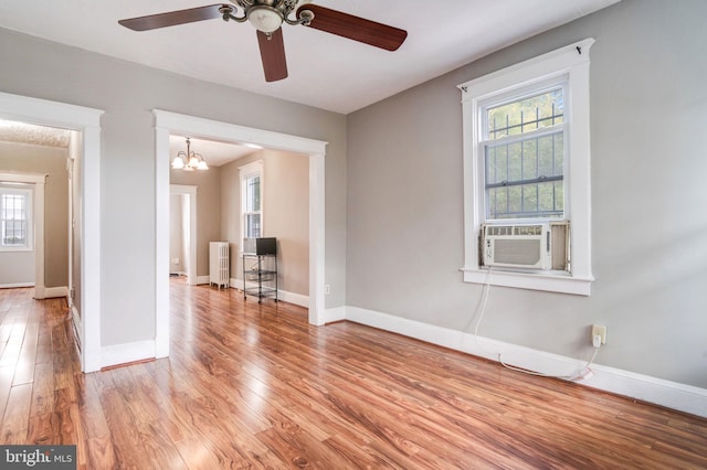 empty room featuring radiator heating unit, light hardwood / wood-style floors, ceiling fan with notable chandelier, and a healthy amount of sunlight