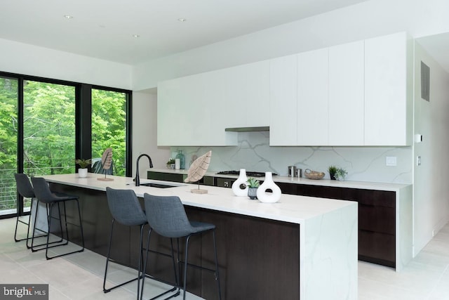 kitchen with decorative backsplash, sink, an island with sink, and white cabinets