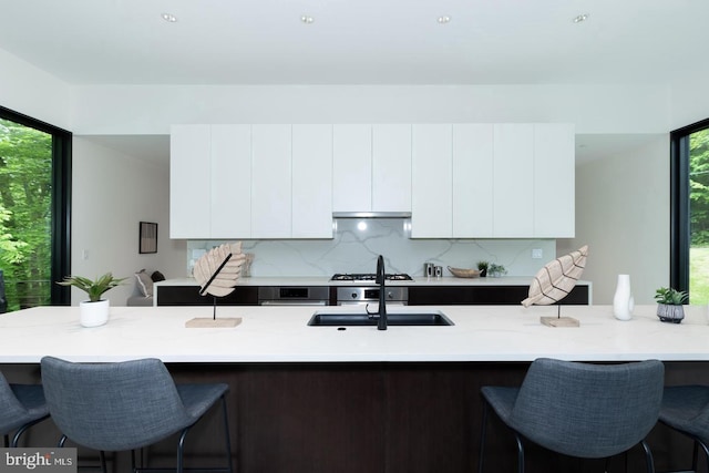 kitchen with light stone countertops, sink, backsplash, white cabinets, and a breakfast bar