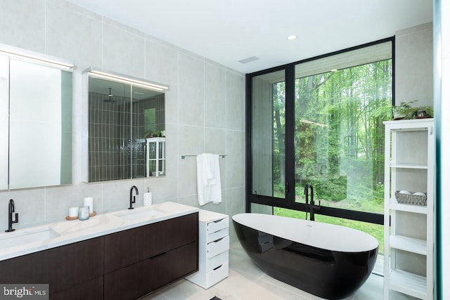full bathroom with tile walls, a freestanding tub, double vanity, and a sink