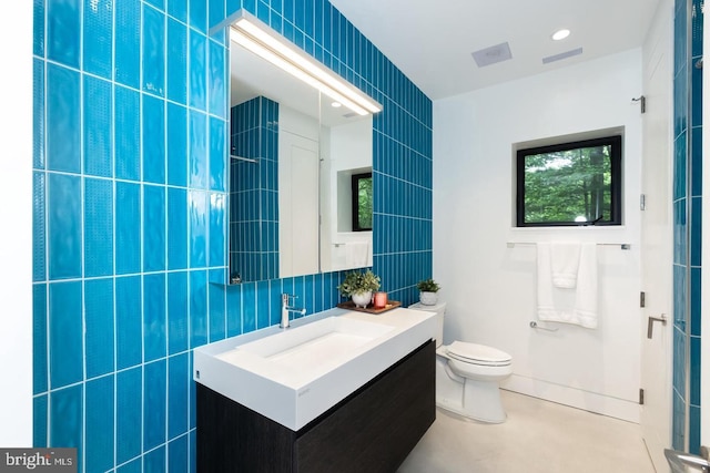 bathroom with vanity, toilet, and tile walls