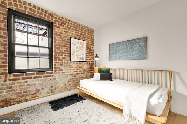 bedroom featuring wood-type flooring and brick wall