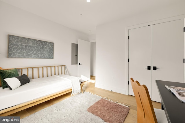 bedroom with light hardwood / wood-style floors, electric panel, and a closet