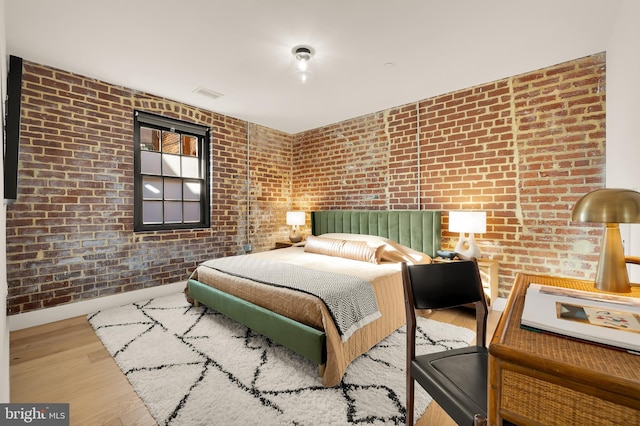 unfurnished bedroom featuring hardwood / wood-style floors and brick wall