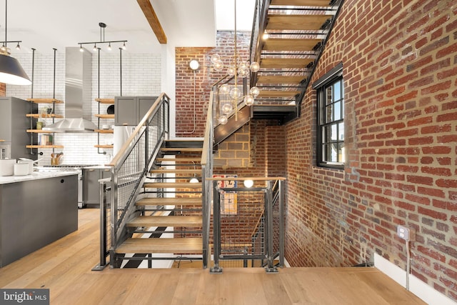 staircase featuring hardwood / wood-style floors, beamed ceiling, and brick wall