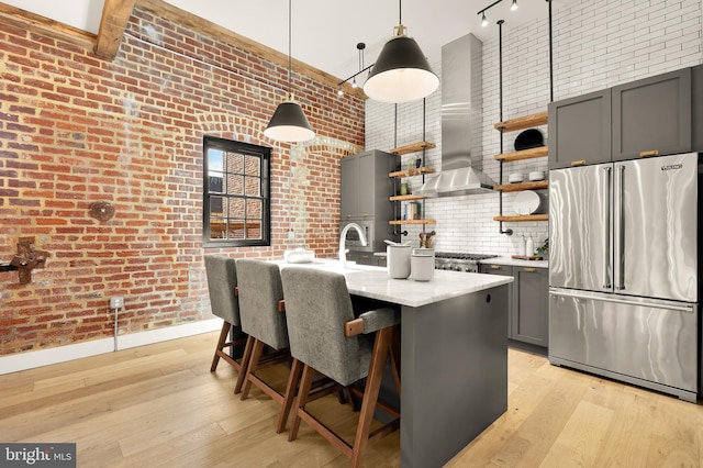 kitchen with pendant lighting, brick wall, exhaust hood, light stone counters, and high end fridge