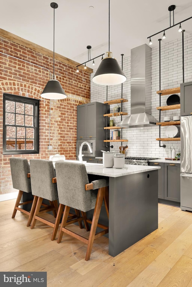 kitchen with exhaust hood, gray cabinets, brick wall, and hanging light fixtures