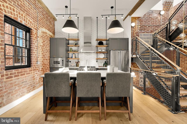 interior space with brick wall, wall chimney range hood, decorative light fixtures, a breakfast bar, and stainless steel appliances