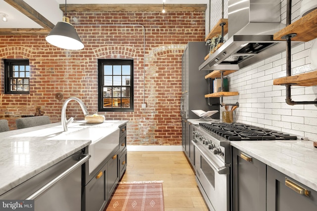 kitchen featuring range hood, brick wall, pendant lighting, stainless steel appliances, and light stone counters