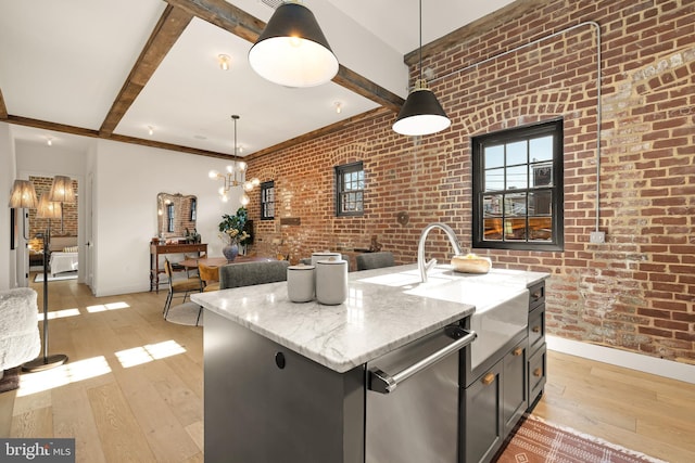 kitchen featuring dishwasher, hanging light fixtures, light stone counters, brick wall, and an island with sink