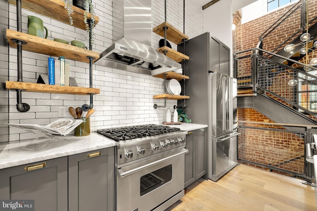 kitchen with light stone countertops, high end stainless steel range, wall chimney exhaust hood, and gray cabinetry