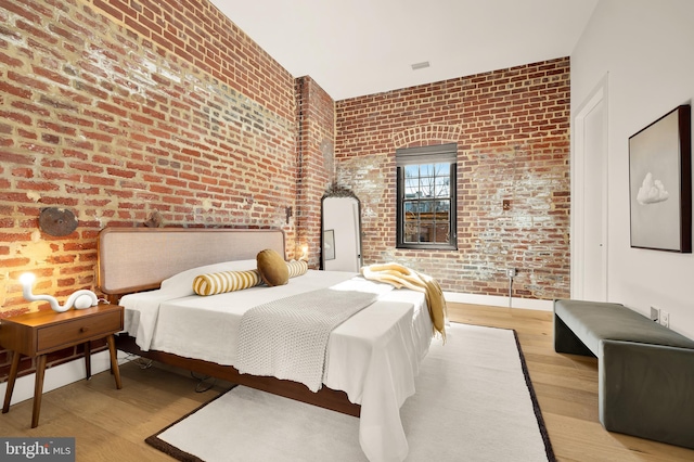 bedroom with brick wall and light hardwood / wood-style flooring