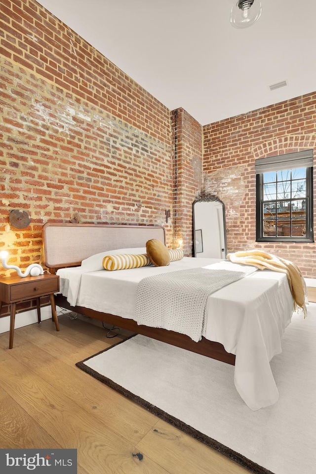 bedroom with wood-type flooring and brick wall