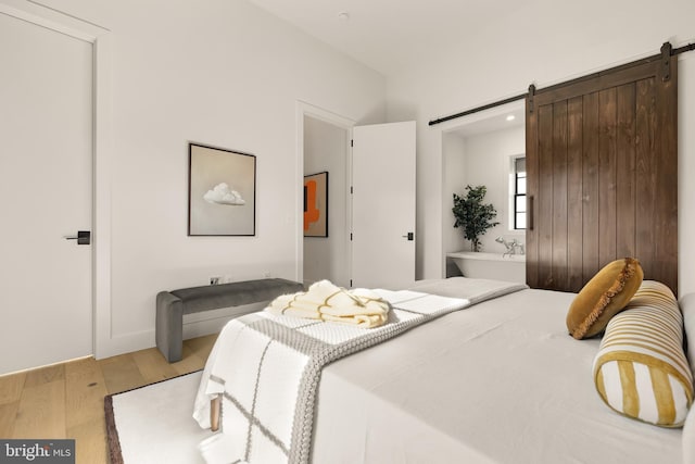 bedroom featuring light wood-type flooring, ensuite bathroom, and a barn door