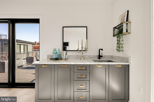 bar with light stone countertops, sink, gray cabinetry, and light hardwood / wood-style flooring