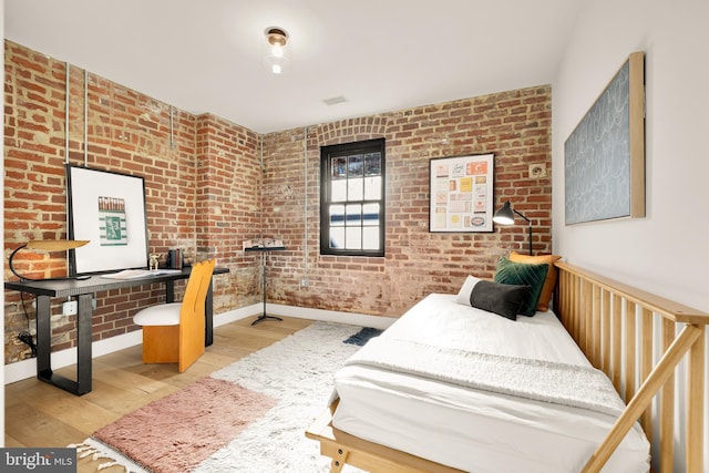 bedroom featuring light hardwood / wood-style floors and brick wall