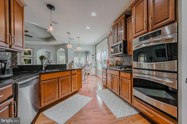 kitchen featuring hanging light fixtures, backsplash, light wood-type flooring, appliances with stainless steel finishes, and dark stone countertops