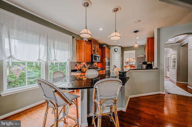 kitchen with stainless steel appliances, wood-type flooring, backsplash, and decorative light fixtures