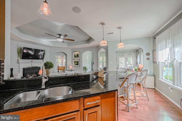 kitchen featuring sink, dark stone countertops, decorative light fixtures, a raised ceiling, and light hardwood / wood-style flooring