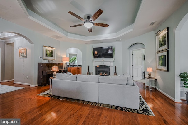 living room featuring ceiling fan, dark hardwood / wood-style floors, and a tray ceiling