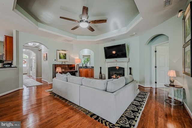 living room with ceiling fan, dark hardwood / wood-style flooring, and a tray ceiling