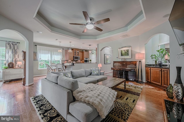 living room featuring ceiling fan, light hardwood / wood-style floors, and a raised ceiling