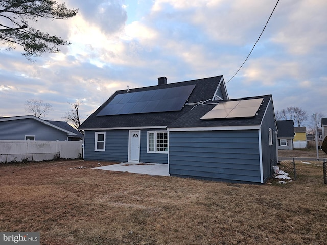 rear view of house featuring a patio area, a lawn, and solar panels