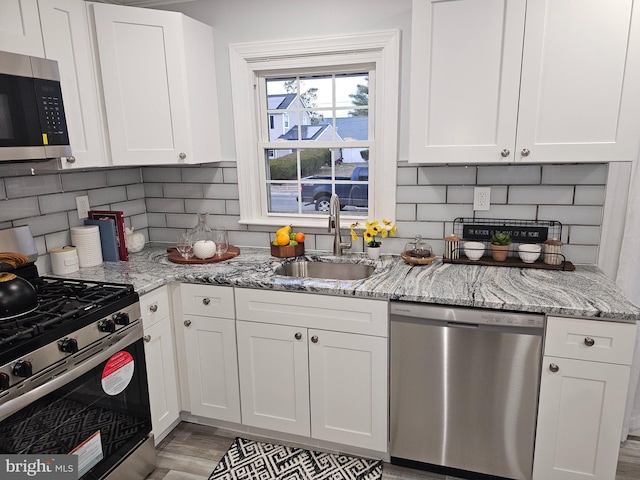 kitchen with light stone countertops, sink, white cabinets, and appliances with stainless steel finishes