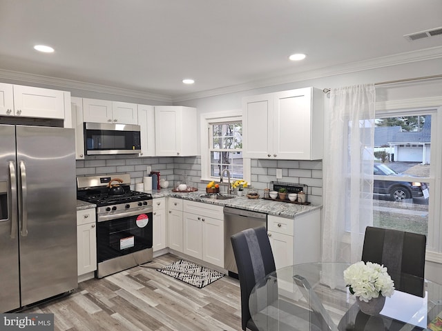 kitchen featuring appliances with stainless steel finishes, backsplash, white cabinets, light stone counters, and sink