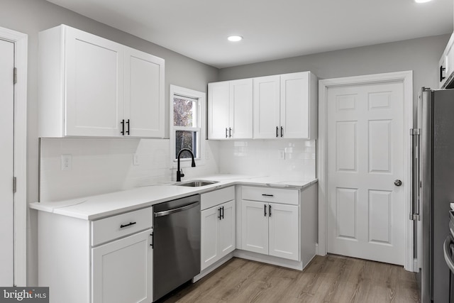 kitchen with appliances with stainless steel finishes, light wood-type flooring, tasteful backsplash, sink, and white cabinetry