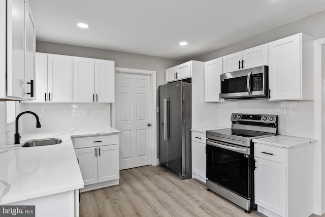 kitchen with appliances with stainless steel finishes, light stone counters, sink, white cabinets, and light hardwood / wood-style floors