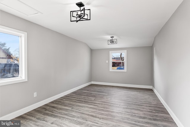 spare room featuring lofted ceiling, a healthy amount of sunlight, wood-type flooring, and a chandelier