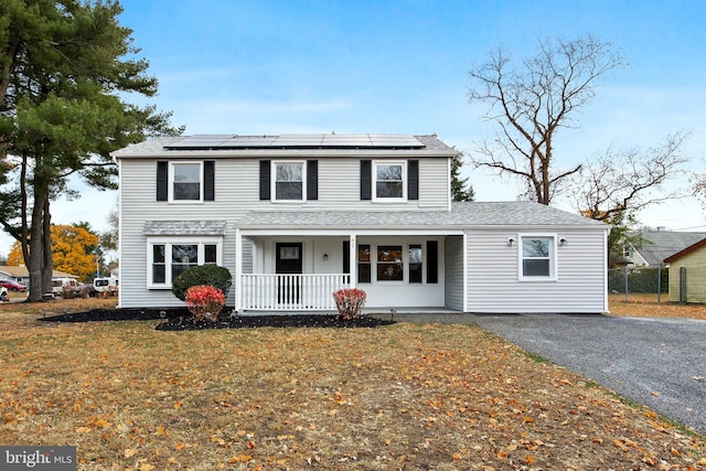 view of front facade featuring covered porch, solar panels, and a front lawn