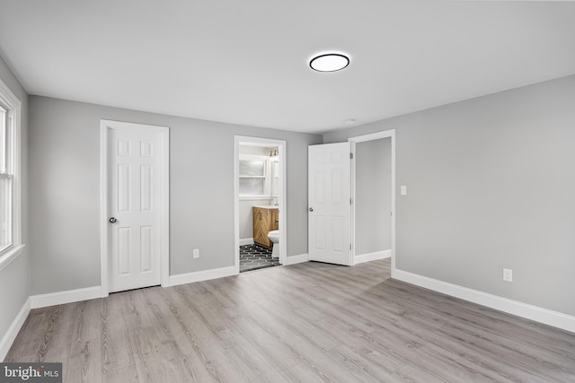 unfurnished bedroom featuring light wood-type flooring, ensuite bath, and a closet