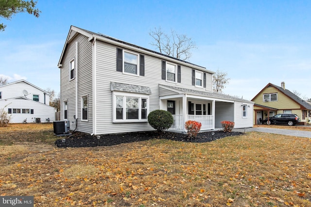 front facade featuring a porch, central air condition unit, and a front lawn