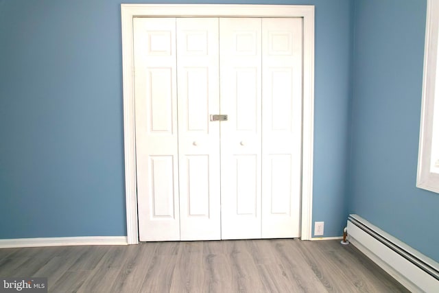 unfurnished bedroom featuring a baseboard radiator, wood-type flooring, and a closet