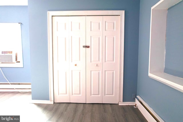 unfurnished bedroom featuring cooling unit, a closet, dark hardwood / wood-style floors, and a baseboard heating unit