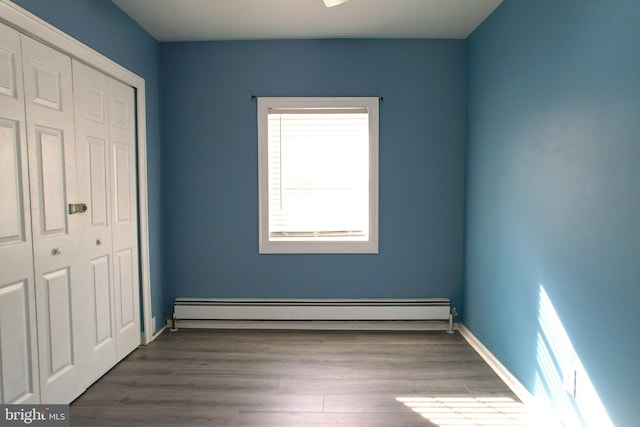 unfurnished bedroom with baseboard heating, a closet, and dark hardwood / wood-style flooring