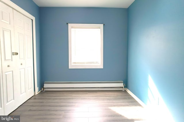 unfurnished bedroom featuring a closet, a baseboard radiator, and hardwood / wood-style floors